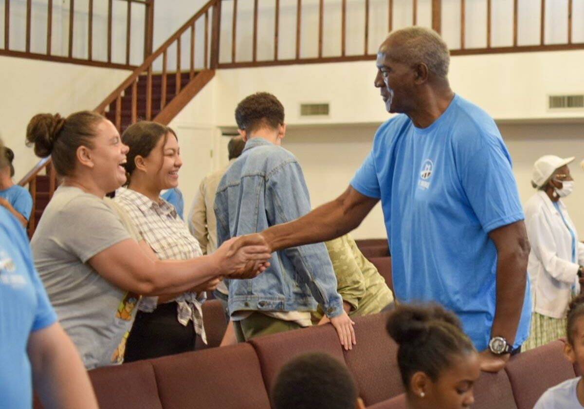inside the sanctuary with an usher in a blue t-shirt greeting two guests dressed casually